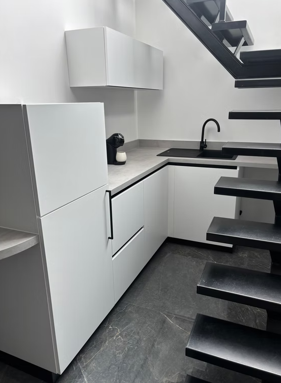 Cuisine blanche sur mesure aménagée sous un escalier métallique